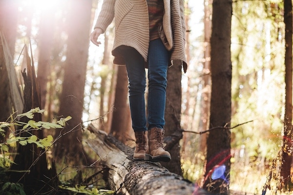 a person wearing boots walking on a tree log with trees in the background.